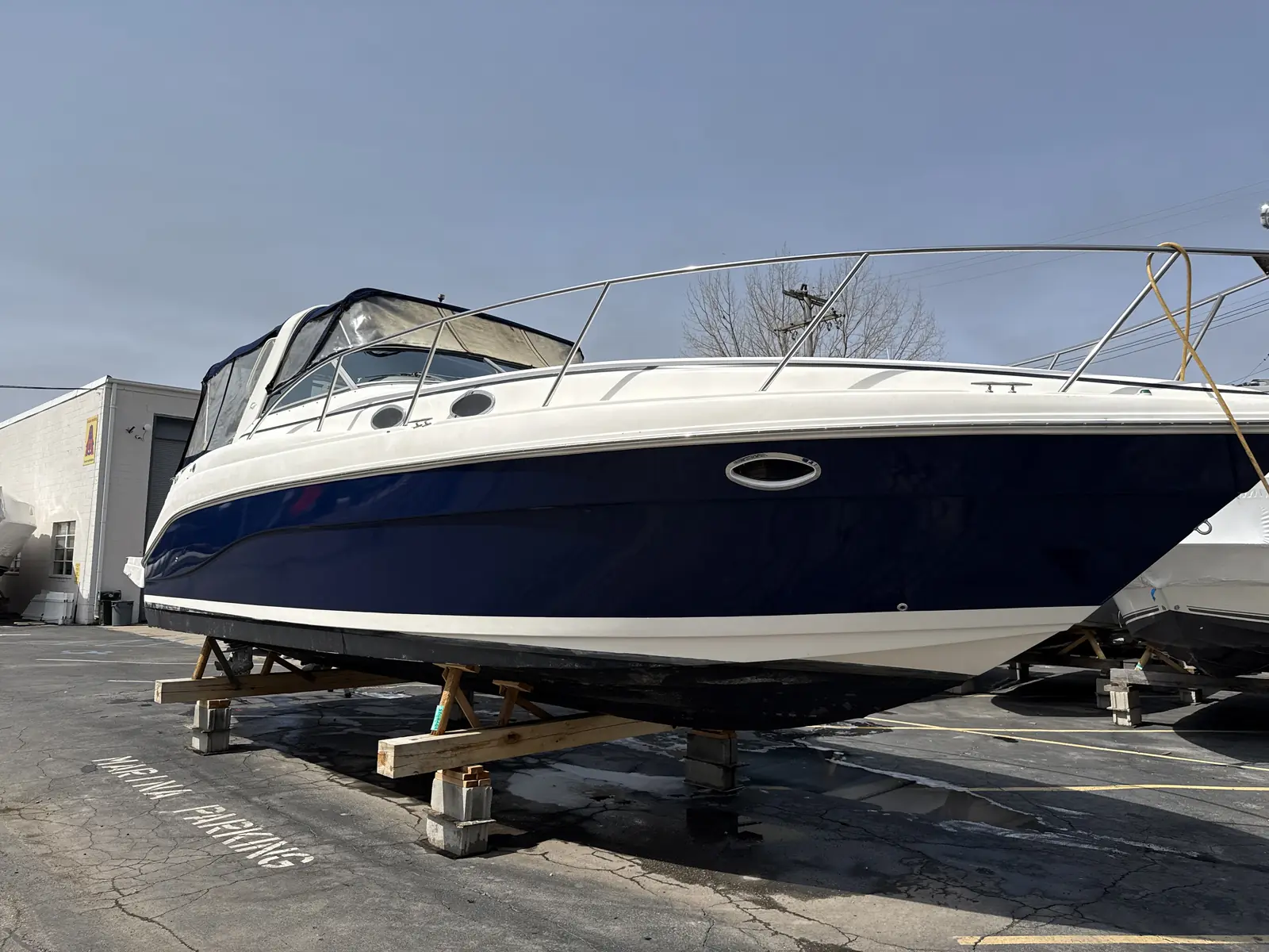 Bow of a navy cabin cruiser on blocks with a bright sky behind it