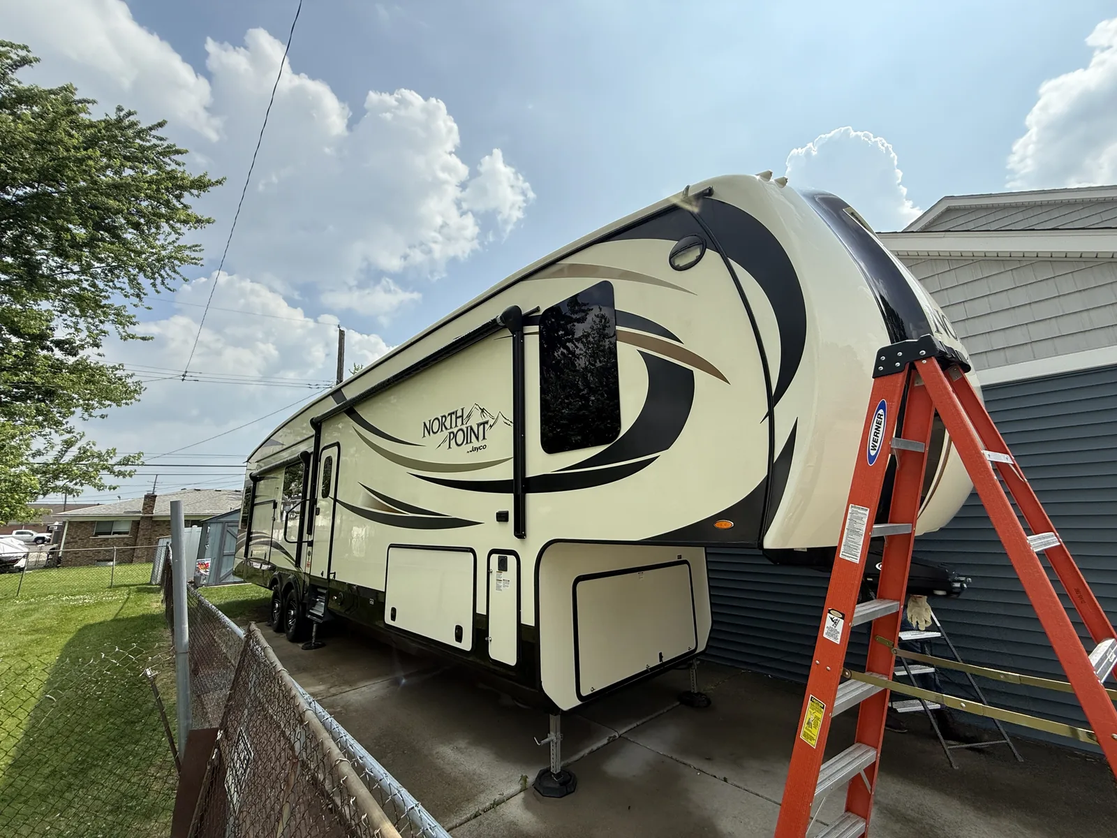 Fifth-wheel RV beside a house with a ladder against it