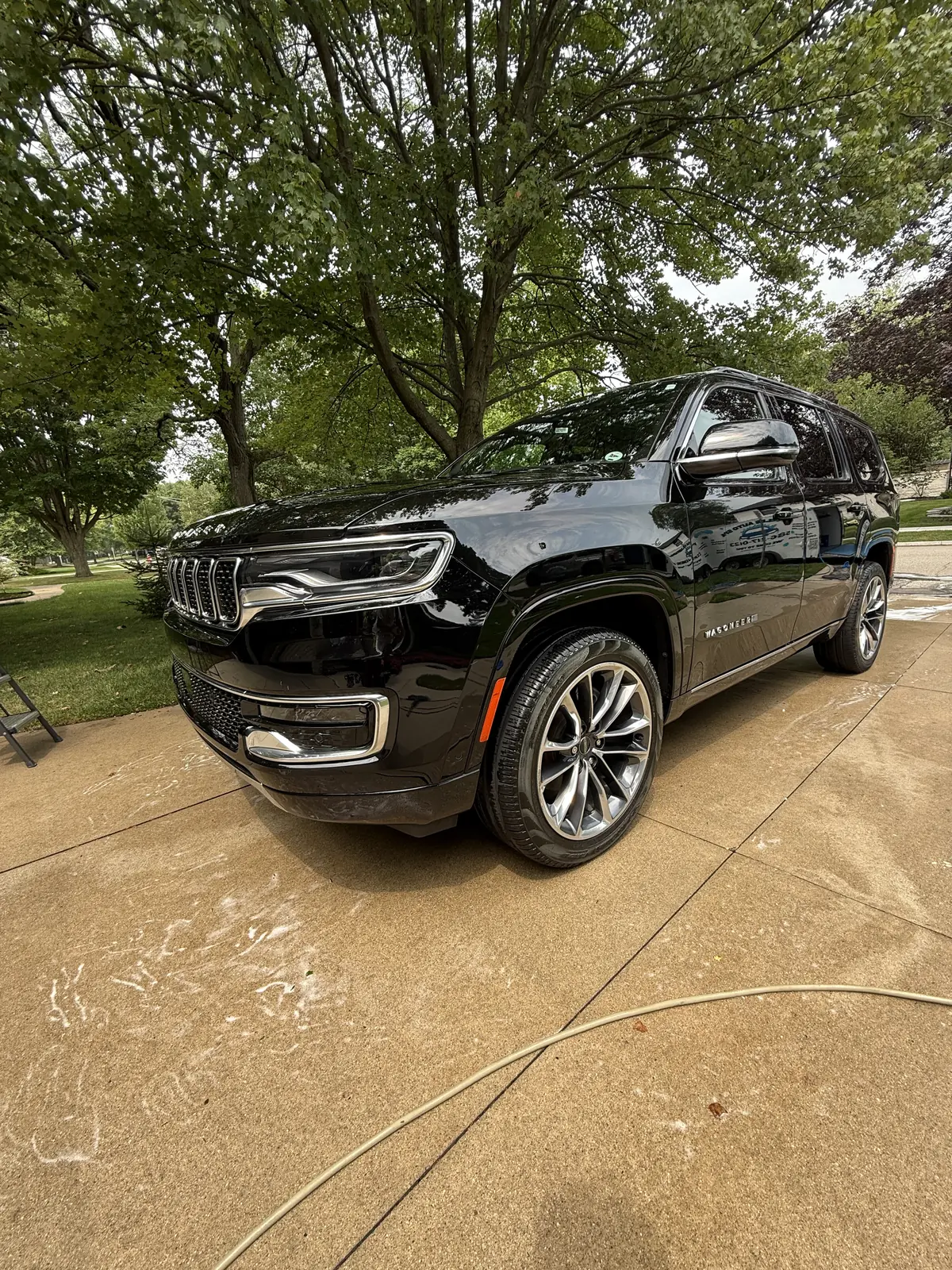 Black Jeep Grand Wagoneer with water beading on the paint in a driveway